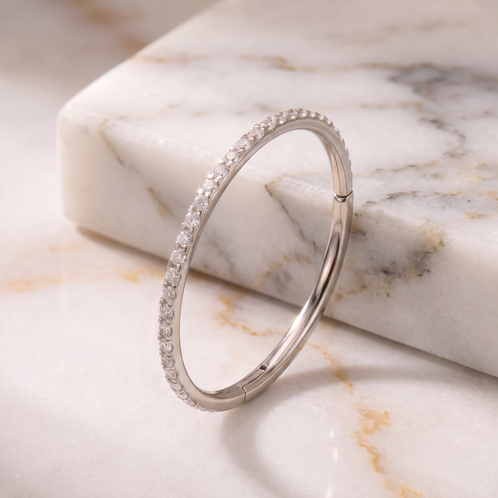 A slim silver-toned huggie ring bracelet with a single row of clear pavé stones, displayed on a white marble slab.