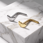 Two modern, sculptural metal wall hooks shaped like golf clubs, one polished silver and one polished gold, displayed on a white marble block.