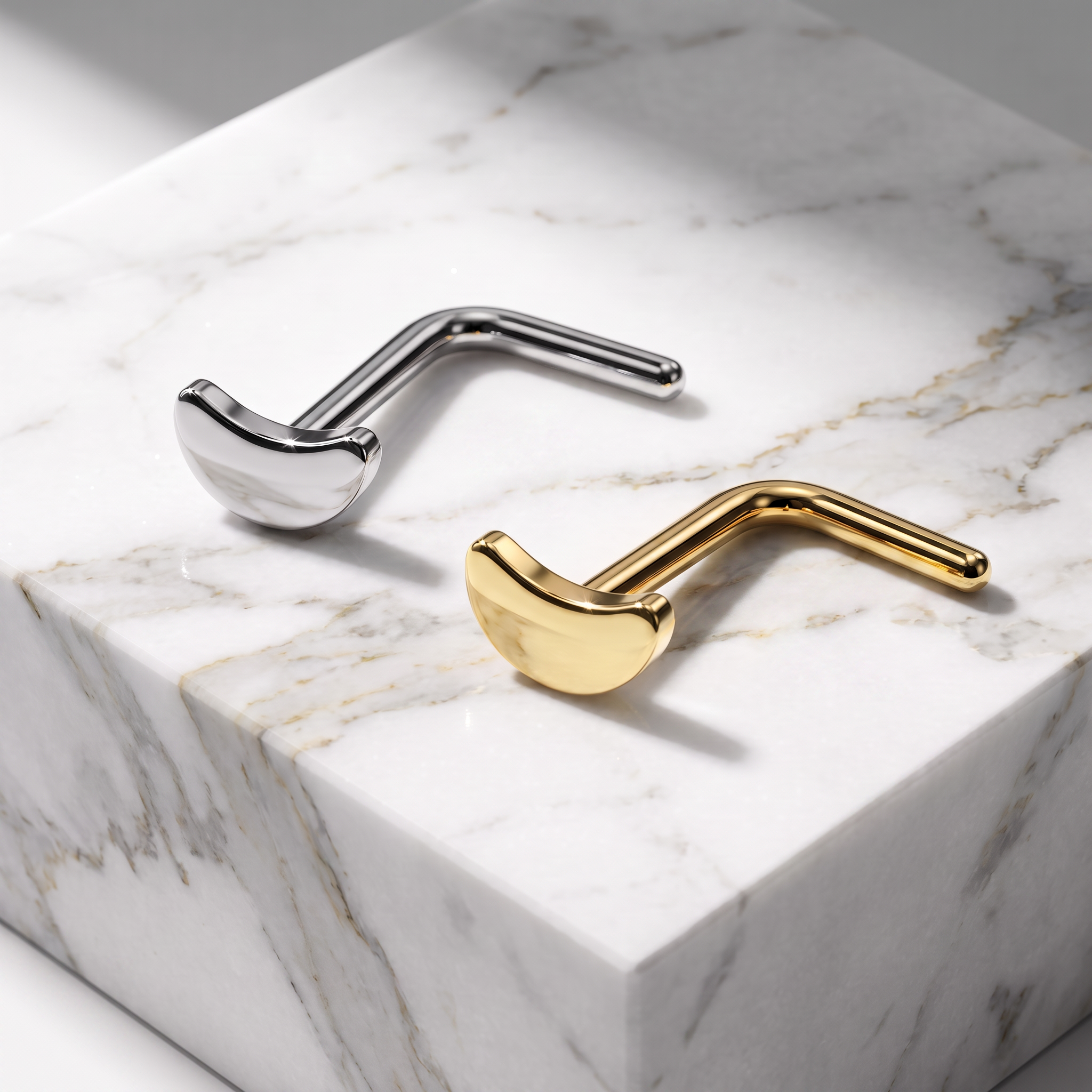 Two modern, sculptural metal wall hooks shaped like golf clubs, one polished silver and one polished gold, displayed on a white marble block.