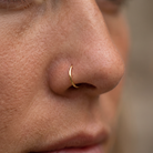 A close-up of a person's nose wearing a thin, polished gold crescent-shaped nose ring.