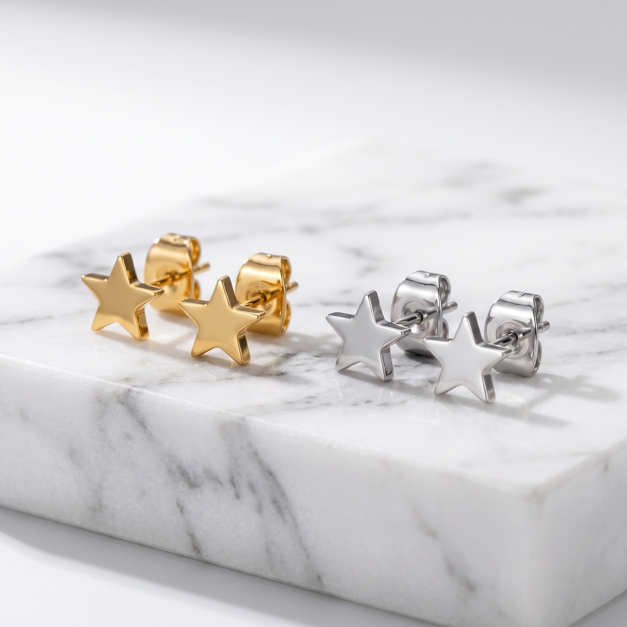 Two pairs of star-shaped stud earrings displayed on a white marble slab. One pair is gold-toned and the other is silver-toned, photographed against a clean white background.