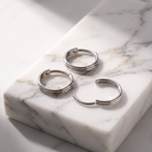 Three silver hoop earrings with a triple-band design, displayed on a white marble block with gray veining.