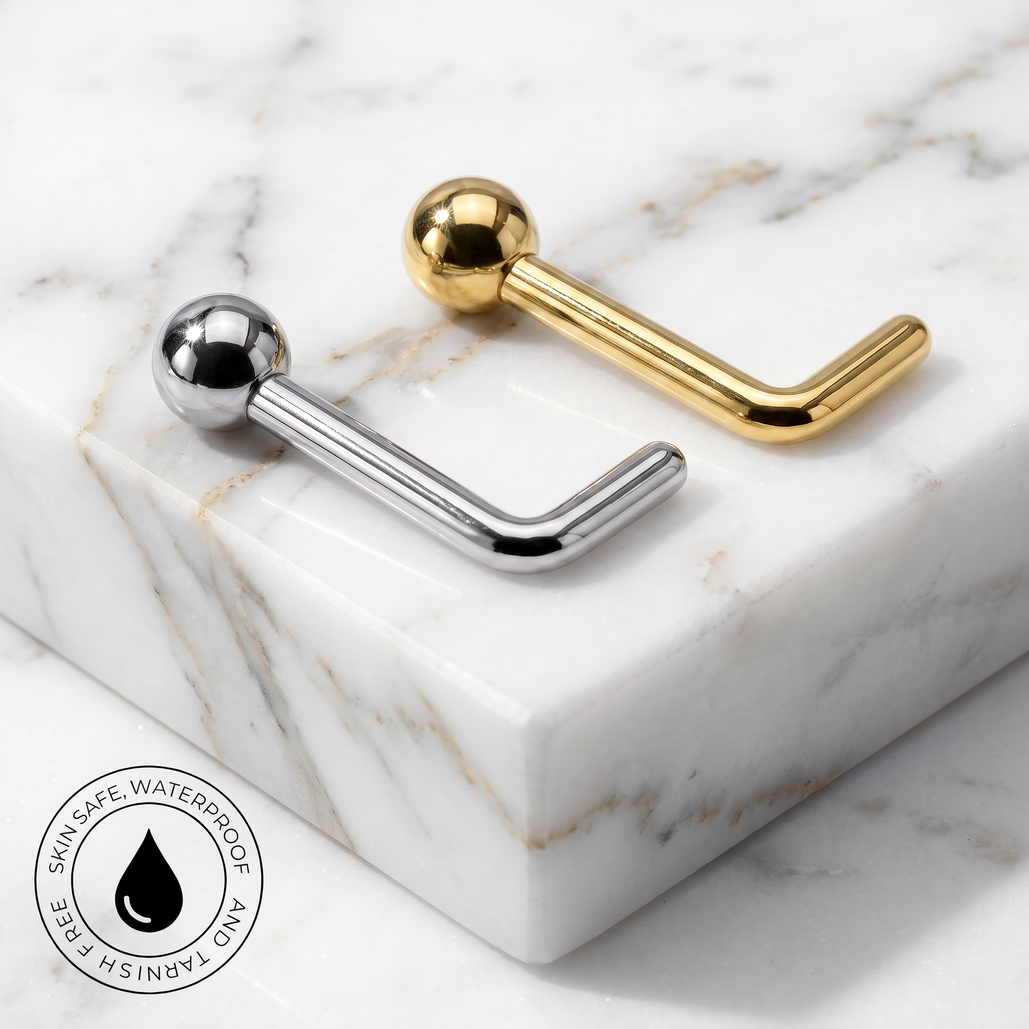 Two curved barbell-style body jewelry pieces with spherical ends, one polished silver and one polished gold, displayed on a white marble block. A circular badge in the lower-left corner reads 'SKIN SAFE WATERPROOF' with a droplet icon.