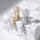 Two flower-shaped cartilage piercings, one in yellow gold and one in silver, both adorned with clear cubic zirconia stones, displayed on a white marble block.