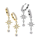 Four dangle hoop earrings shown on a plain white background: two in yellow gold and two in silver, each featuring a pavé-set hoop, a starburst charm, and a dangling round clear stone.