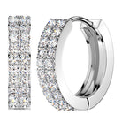 A pair of silver-toned huggie hoop earrings paved with round clear stones, shown on a plain white background with one earring viewed from the side and the other from the front.