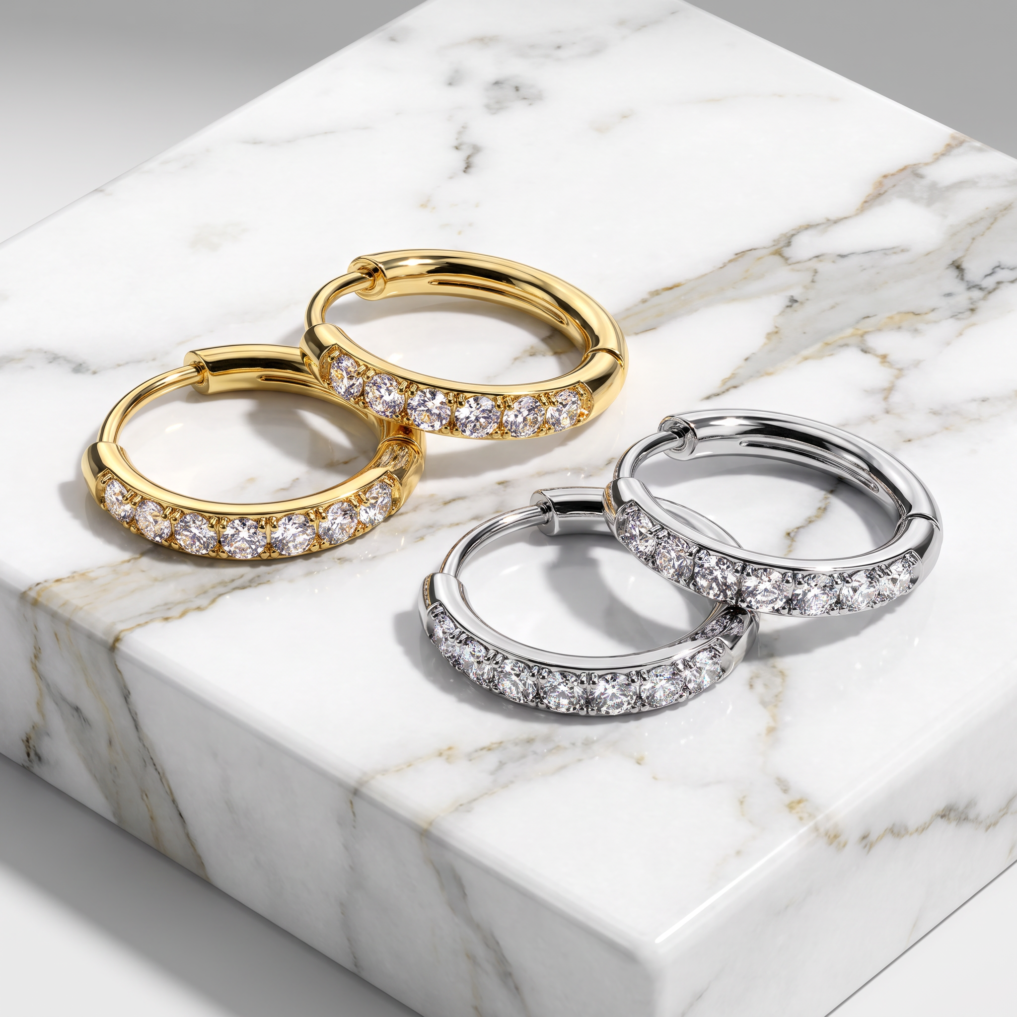 Two pairs of huggie hoop earrings with pavé-set clear stones, shown in yellow gold and silver-tone metal on a white marble slab.
