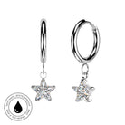 A pair of silver huggie hoop earrings with dangling star-shaped clear crystals, shown on a white background with a circular 'skin-safe waterproof' badge in the lower left.