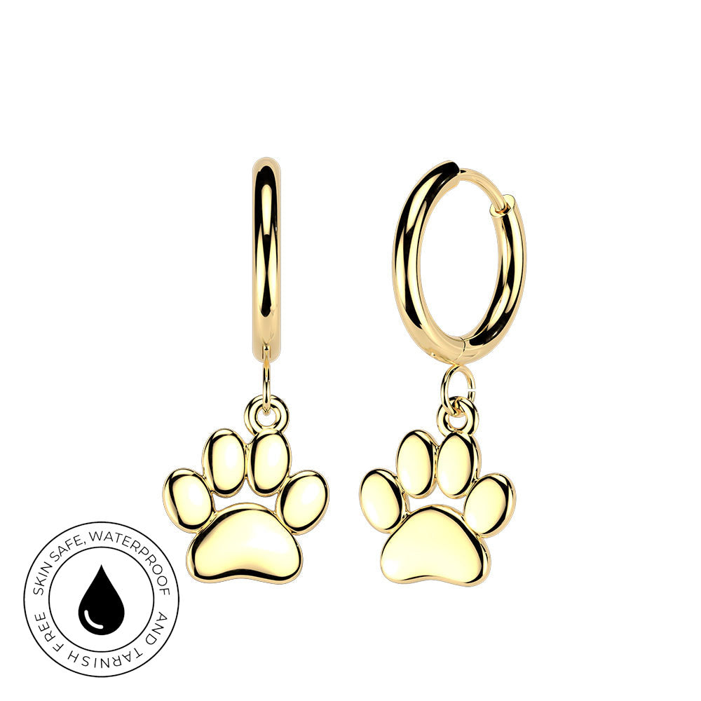 A pair of gold-toned huggie hoop earrings with dangling paw print charms, shown on a plain white background. A circular badge in the lower-left corner indicates skin-safe waterproof and tarnish-free features.