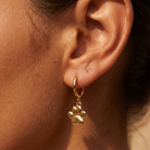 A close-up of a person's ear wearing a gold hoop earring with a dangling paw print charm.