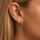 A close-up of a model's ear wearing a small gold huggie hoop earring.