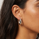 A close-up of a model's ear wearing a polished silver hoop earring.