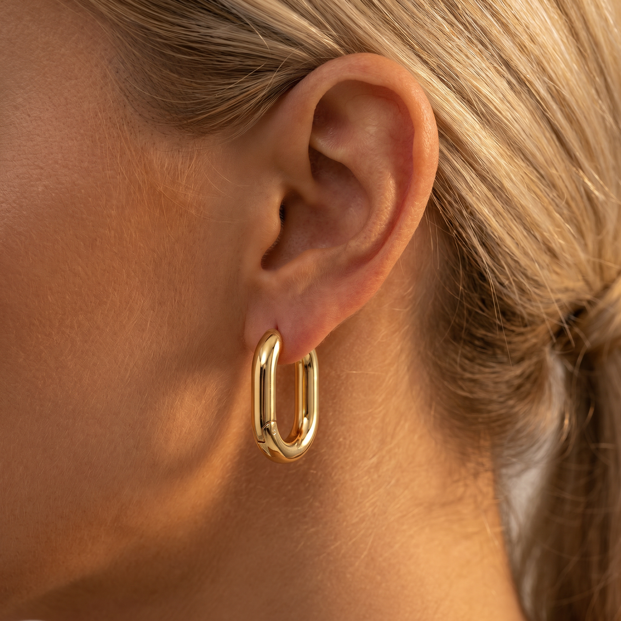 A close-up of a model's ear wearing a polished gold huggie hoop earring.
