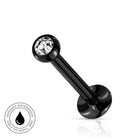 A black labret piercing barbell with a clear faceted gemstone in the ball end, shown on a white background with a small circular 'SkinSafe Waterproof' badge in the lower-left corner.