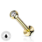 A gold-plated curved barbell piercing stud with a clear faceted gemstone in the top ball, shown on a white background with a small circular 'skin-safe waterproof' badge in the lower-left corner.