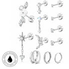 A set of silver-colored stud earrings and hoop earrings with clear crystals, displayed on a clean white background. The collection includes various designs such as a flower with leaves, a dangling star with a heart, a crescent moon, and multiple styles of hoop earrings, some adorned with small crystals.