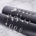 A set of silver-toned body jewelry displayed on dark gray velvet rings, including studs, earrings, and a flower-shaped stud, photographed on a light marble surface.