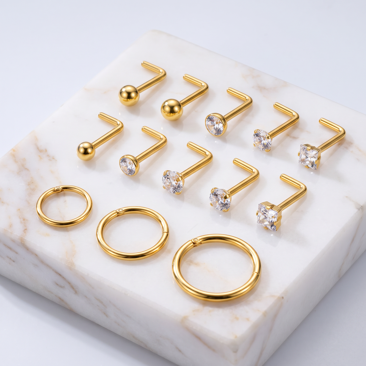 Gold body jewelry set displayed on a white marble slab, featuring multiple straight barbells with clear gemstones and three matching curved hoop rings.