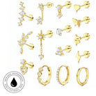 A collection of gold-colored stud earrings and hoop earrings with clear crystals, arranged on a white background. The designs include stars, leaves, hearts, butterflies, snakes, lightning bolts, and geometric patterns.