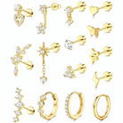 A collection of gold-plated stud earrings and hoop earrings with clear crystals, arranged on a plain white background. The designs include hearts, stars, leaves, snakes, lightning bolts, and huggie hoops.