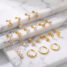 A set of gold-colored stud earrings and hoop earrings with clear crystal accents, arranged on a white marble background.