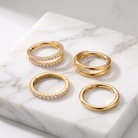Four gold hoop earrings displayed on a white marble slab. Two hoops are adorned with small clear stones, and the remaining two are solid gold.