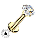A gold-plated labret piercing barbell with a large, clear, cushion-cut gemstone on a plain white background. A circular graphic overlay in the bottom-left corner features a water droplet icon and the text 'SKIN SAFE WATERPROOF AND TARNISH FREE'.