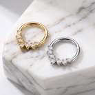 Two hoop earrings with marquise-cut clear crystals are displayed on a white marble block. One earring has a gold-tone metal body, and the other has a silver-tone metal body.