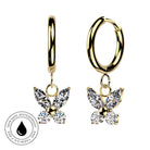 A pair of gold hoop earrings with butterfly charms set with clear marquise and round gemstones, shown on a white background with a circular skin-safe waterproof badge in the lower left.