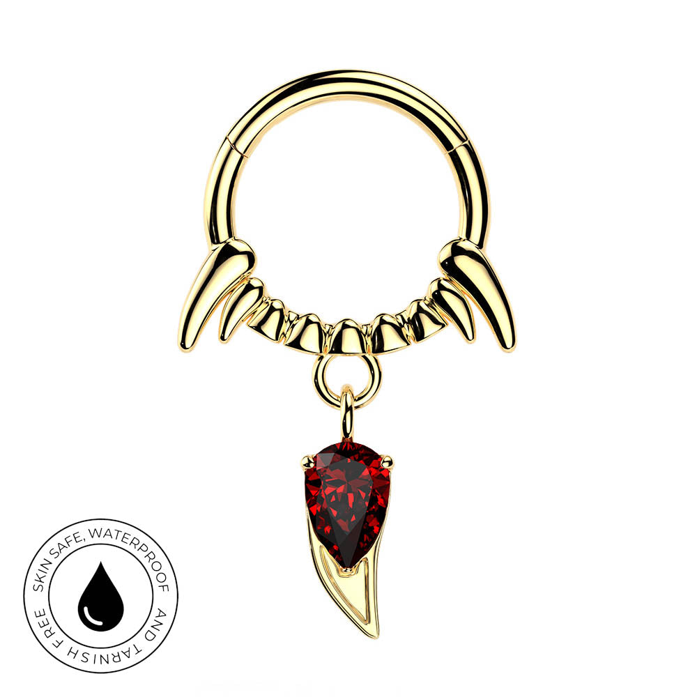 Gold-toned piercing ring with curved claw-like prongs and a dangling red teardrop gemstone, shown on a white background with a circular skin-safe waterproof badge in the lower left.