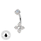 A curved barbell belly button ring with a flower-shaped dangling charm, both set with clear round gemstones in a silver-toned metal. A circular badge in the bottom-left corner reads 'SKIN SAFE WATERPROOF' with a black droplet symbol.