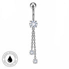 Silver-toned navel barbell piercing with a large clear crystal flower at the belly button, two dangling chain links, and three smaller clear crystal flowers, shown on a white background with a circular 'skin-safe waterproof' badge in the lower left.