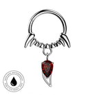 A silver-toned piercing ring with curved claw-like extensions and a dangling red teardrop gemstone, shown on a plain white background with a circular 'skin-safe waterproof and tarushi free' badge in the lower left.